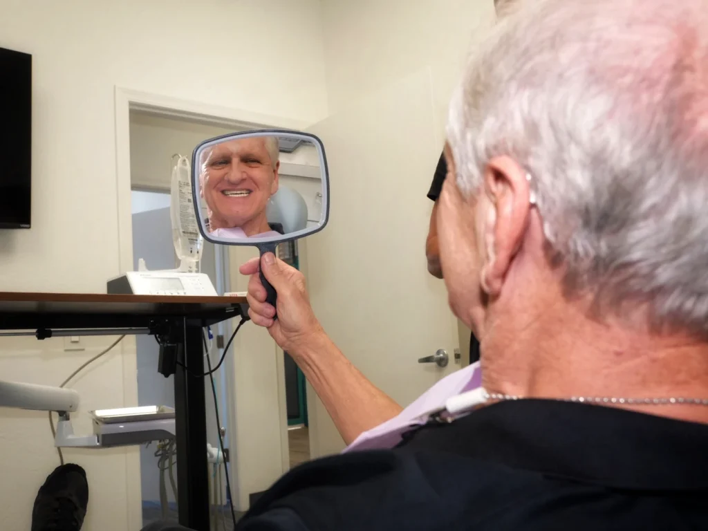 Happy patient smiling in mirror after dental implants in Mesa, AZ at Mesa Dental Implants and Dentures
