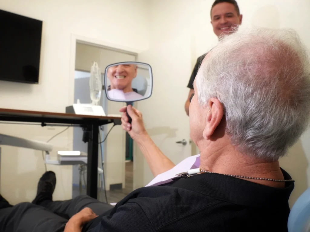 Happy patient smiling in mirror after dental implants in Mesa, AZ at Mesa Dental Implants and Dentures